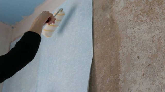 A sheet of blue papper wallpaper is glued to the wall with a special construction roller