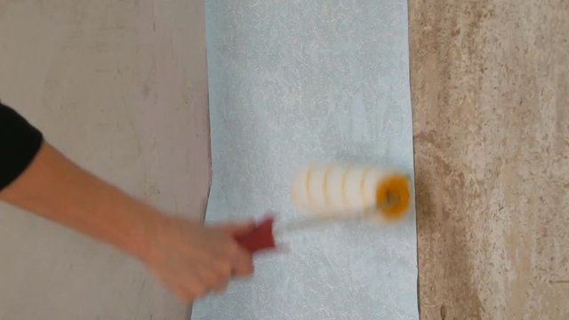 A sheet of blue papper wallpaper is glued to the wall with a special construction roller
