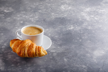 Cup of coffee and freshly baked croissants on gray background. Copy space.