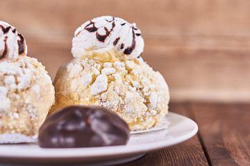 Two airy desserts with meringue in chocolate drops with prunes and butter cream and the chocolate zephyr in a white plate on a wooden background