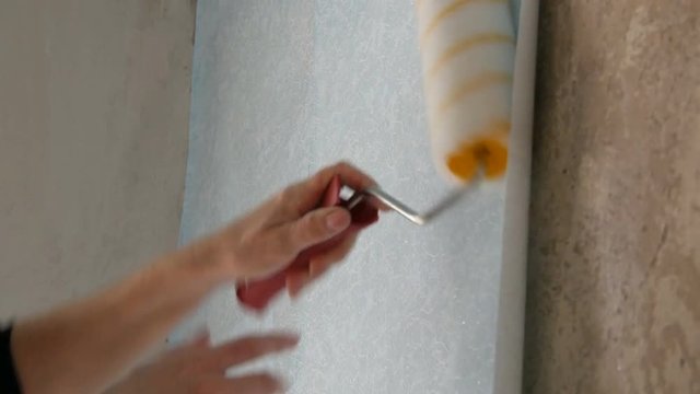 A sheet of blue papper wallpaper is glued to the wall with a special construction roller