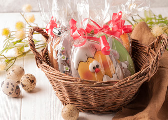 easter cookies in a brown wicker basket near quail eggs and blossoming branch on wooden white surface