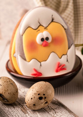 easter cookie with painted hatched chicken in dark bowl near quail eggs on white wooden surface