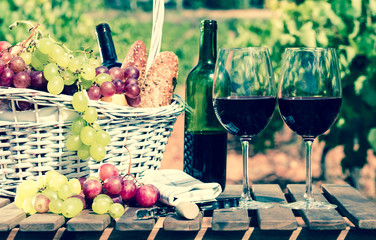 glass of red wine grapes and picnic basket on table in field