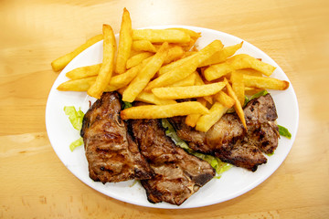 Grilled lamb ribs with french fries on a plate on a wooden table