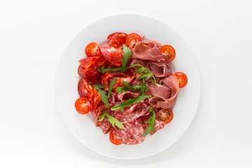 Cold meat plate with ham, proscuitto and salami served with cherry tomatoes top view on a white background. Spanish meat tapas or italian antipasti