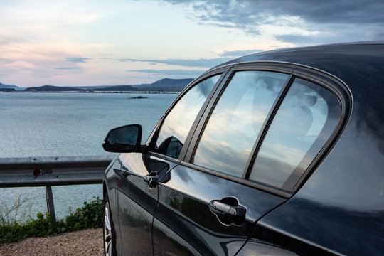 Rear View Of Modern Luxury Black Car Parked Above The Sea With A Romantic View During The Sunset