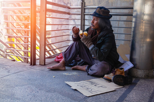 Homeless man is sitting down on walkway in town. He Eating bread.He is very glad  and happy. poverty, despair, Photo Sympathetic and hope concept.