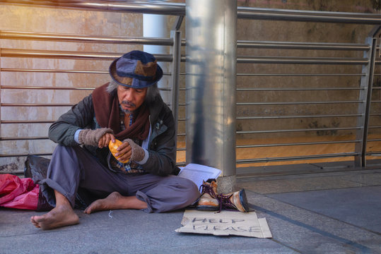 Homeless man is sitting down on walkway in town. He Eating bread.He is very glad  and happy. poverty, despair, Photo Sympathetic and hope concept.