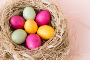 colorful Easter eggs in nest with hay on beige background