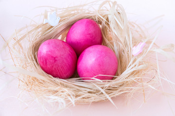 3 pink Easter eggs in nest with hay on beige background, boiled eggs