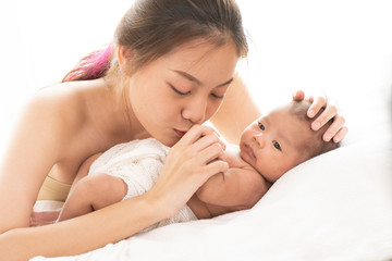pretty happy young asian mom holding her newborn baby with love and care on white background bed