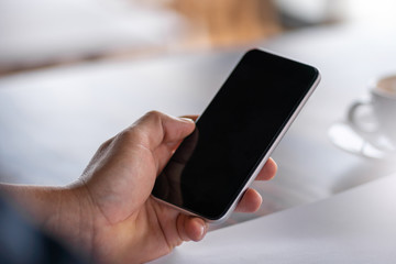 Selective focus of Casual young business man hand using mobile smart phone with coffee blurred background