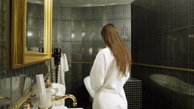 Young woman dressed in white bathrobe preparing to take a bubble bath. 4K
