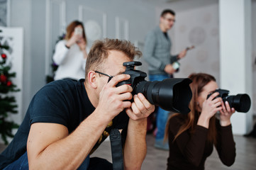 The team of two photographers shooting on studio behind another three workers. Professional...