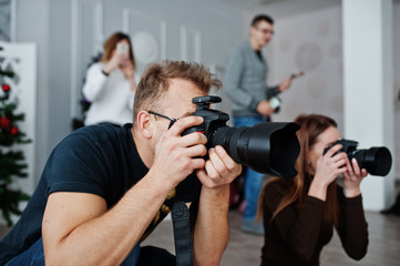 The team of two photographers shooting on studio behind another three workers. Professional photographer on work. Master class.