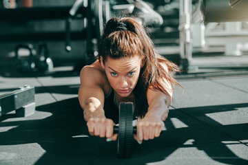 Young attractive sporty female bodybuilder with ponytail doing exercises for abs on gym floor....