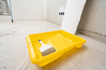 Paintbrush, roller and glue container on concrete surface. Composition tools for home repair and interior renovation indoors.