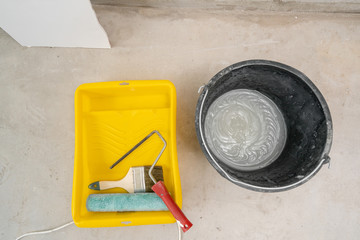 Paintbrush, roller and glue container on concrete surface. Composition tools for home repair and interior renovation indoors.