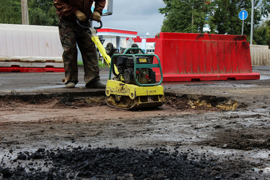 The foreman of the construction team works with a vibrating platform plate, tamping up the sand before the asphalting of the road using the patch method. reportage