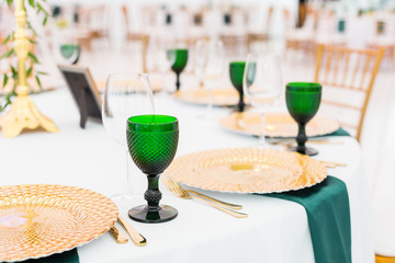 Golden dishes, green wine glasses and napkins. Catering concept. Interior of tent for wedding dinner, ready for guests. Served round banquet table.