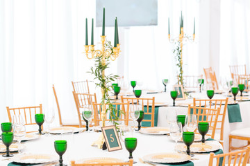 Interior of tent for wedding dinner, ready for guests. Served round banquet table. Golden dishes, green wine glasses and napkins. Catering concept.