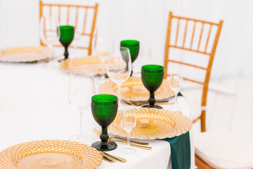 Golden dishes, green wine glasses and napkins. Catering concept. Interior of tent for wedding dinner, ready for guests. Served round banquet table.
