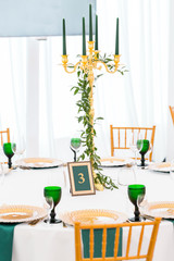 Interior of tent for wedding dinner, ready for guests. Served round banquet table. Golden dishes, green wine glasses and napkins. Catering concept.