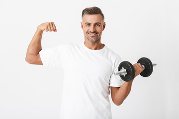 Image of bodybuilder man 30s with bristle wearing casual t-shirt pumping biceps and lifting dumbbell