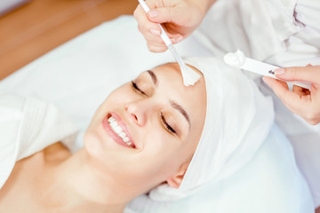 The beautician applies a cleansing mask to the face with a brush. Cosmetic procedure for facial rejuvenation.