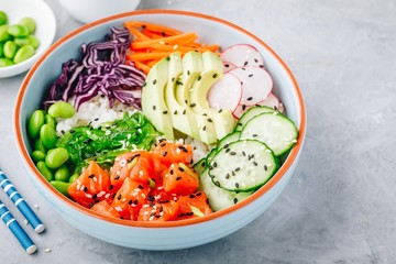 Salmon poke bowl with rice, avocado, seaweed, carrots, cucumber, radishes and edamame beans