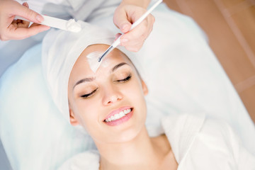 Cosmetology. Cosmetologist applies a cleansing mask on the face with a brush. Cosmetic procedure for facial rejuvenation.