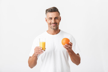 Image of masculine man 30s with bristle wearing casual t-shirt holding glass of juice and orange...