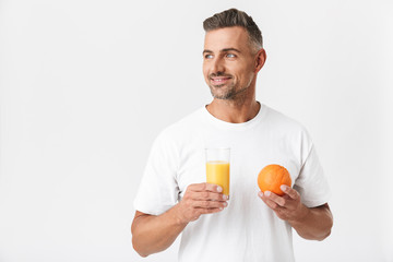 Image of unshaved man 30s with bristle wearing casual t-shirt holding glass of juice and orange...
