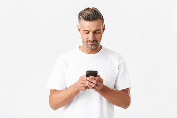 Image of brunette man 30s wearing casual t-shirt holding and using smartphone