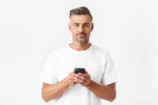 Image of muscular man 30s wearing casual t-shirt holding and using smartphone