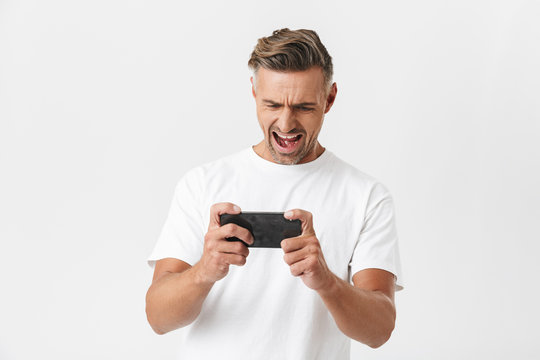 Image of mustached man 30s wearing casual t-shirt using smartphone and playing video games
