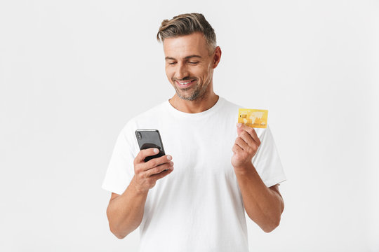 Image of young man 30s wearing casual t-shirt holding smartphone and plastic credit card