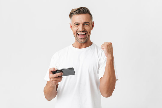 Image of successful man 30s wearing casual t-shirt using smartphone and playing video games