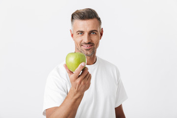 Image of happy man 30s with bristle posing on camera and holding green apple in hand