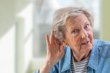 Repeat, please. Close-up of face of charming elderly woman is holding hand by her ear and...