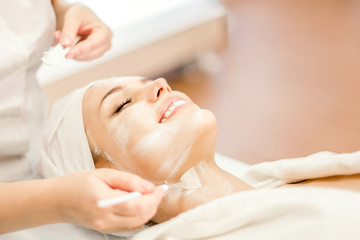 Cosmetology. The hands of a cosmetologist apply a cleansing mask for the face. Smiling girl on...