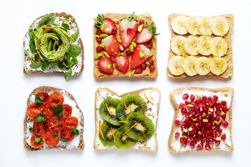 Healthy vegan breakfast concept. Peanut butter sandwiches with strawberry, banana & kiwi toasts, avocado and sun dried tomatoes. White table background. Top view, close up, copy space, flat lay