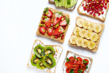 Healthy vegan breakfast concept. Peanut butter sandwiches with strawberry, banana & kiwi toasts, avocado and sun dried tomatoes. White table background. Top view, close up, copy space, flat lay