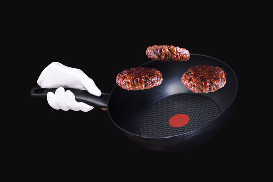 Hand holding Frying pan. White glove holding black pan with fried budger patties in the air isolated on black background.