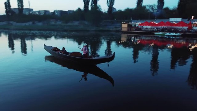 Young woman floating in a boat and holding lantern at night. Traditional venetian rowing boat with the gondolier and a female in the evening river. Camera moves around.
