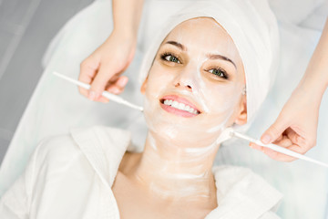 The cosmetologist applies a cleansing face mask with two brushes. Beautiful girl on the procedure for facial rejuvenation. Spa procedure for the face. Cosmetology.