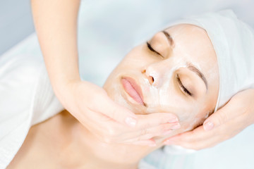 Fototapeta na wymiar Beautician makes facial massage with mask. Beautiful young girl on spa procedure.