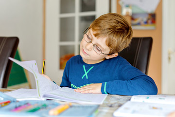 Naklejka na ściany i meble Portrait of cute school kid boy wearing glasses at home making homework. Little concentrated child writing with colorful pencils, indoors. Elementary school and education