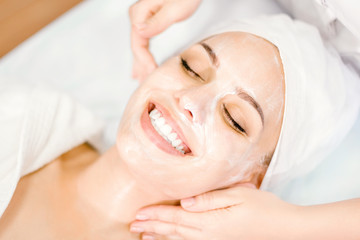 Fototapeta na wymiar Beautician makes facial massage with mask. Beautiful smiling girl on spa procedure.